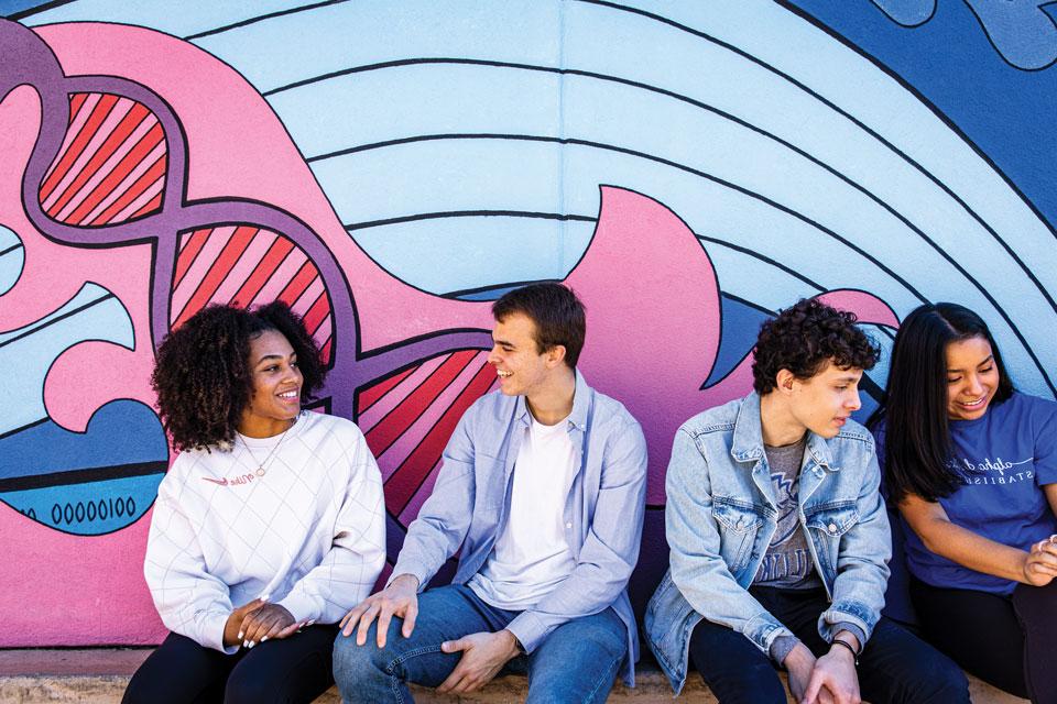 Four 博彩网址大全 students chatting in front of a painted mural